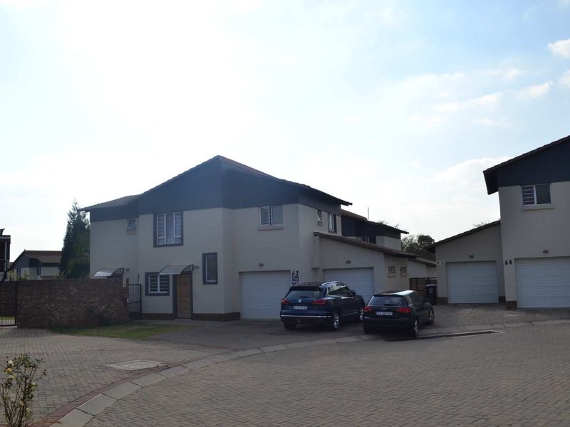 Front exterior view of a residential property featuring a paved driveway, double garage, and brick boundary wall in a secure complex setting.
