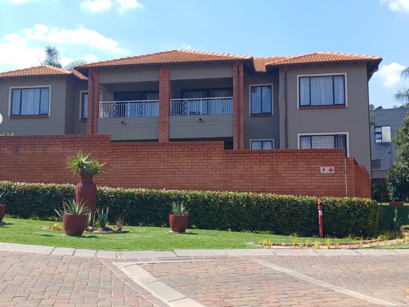Front view of a multi-story townhouse complex featuring a brick boundary wall, tiled roof, and a balcony with metal railings.