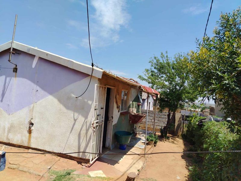 Rear exterior view of the property featuring a small tiled patio area, an external wash basin, and security gate access.
