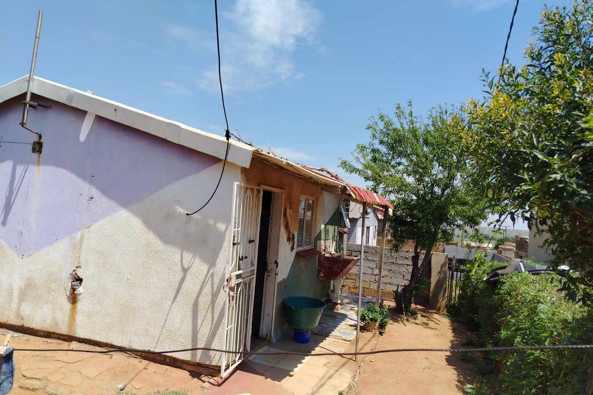 Rear exterior view of the property featuring a small tiled patio area, an external wash basin, and security gate access.