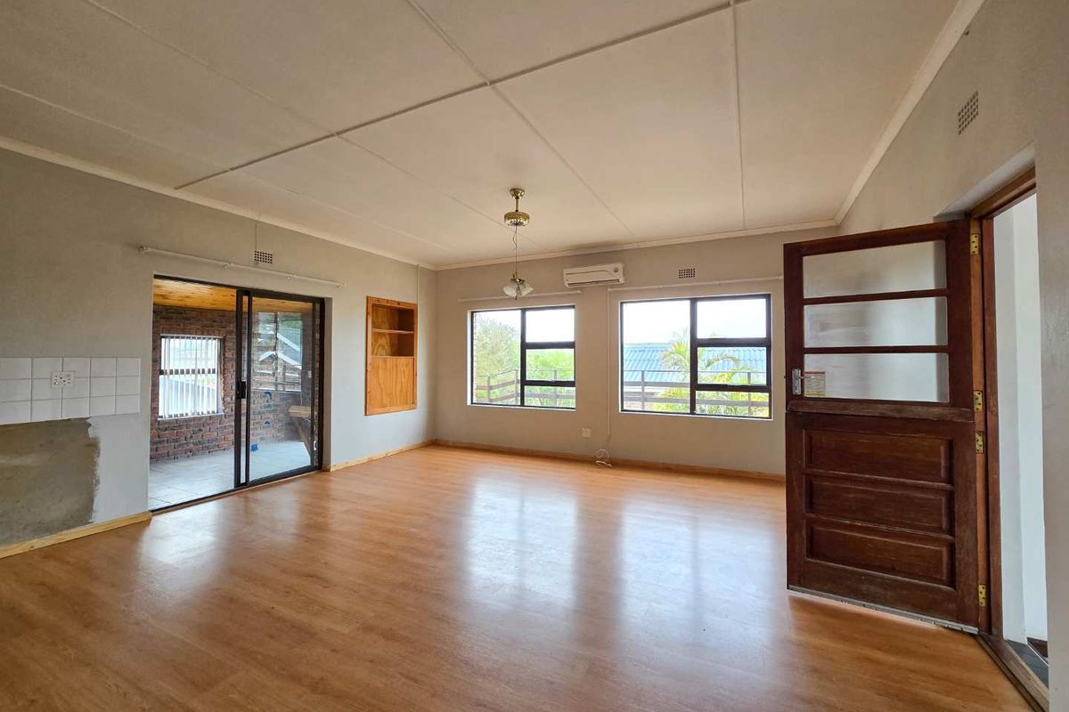 Spacious living area featuring wood-look flooring, large windows for natural light, a built-in wall niche, and direct access to an enclosed patio.