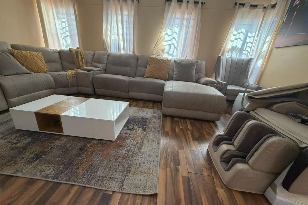 A comfortable living room featuring warm-toned laminate flooring and multiple windows with installed curtain rods, providing a bright and inviting atmosphere.