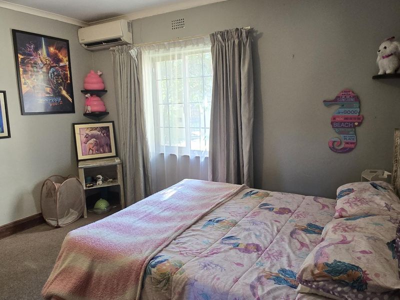 A standard bedroom featuring carpeted flooring, a window with curtains, and a wall-mounted air conditioning unit.