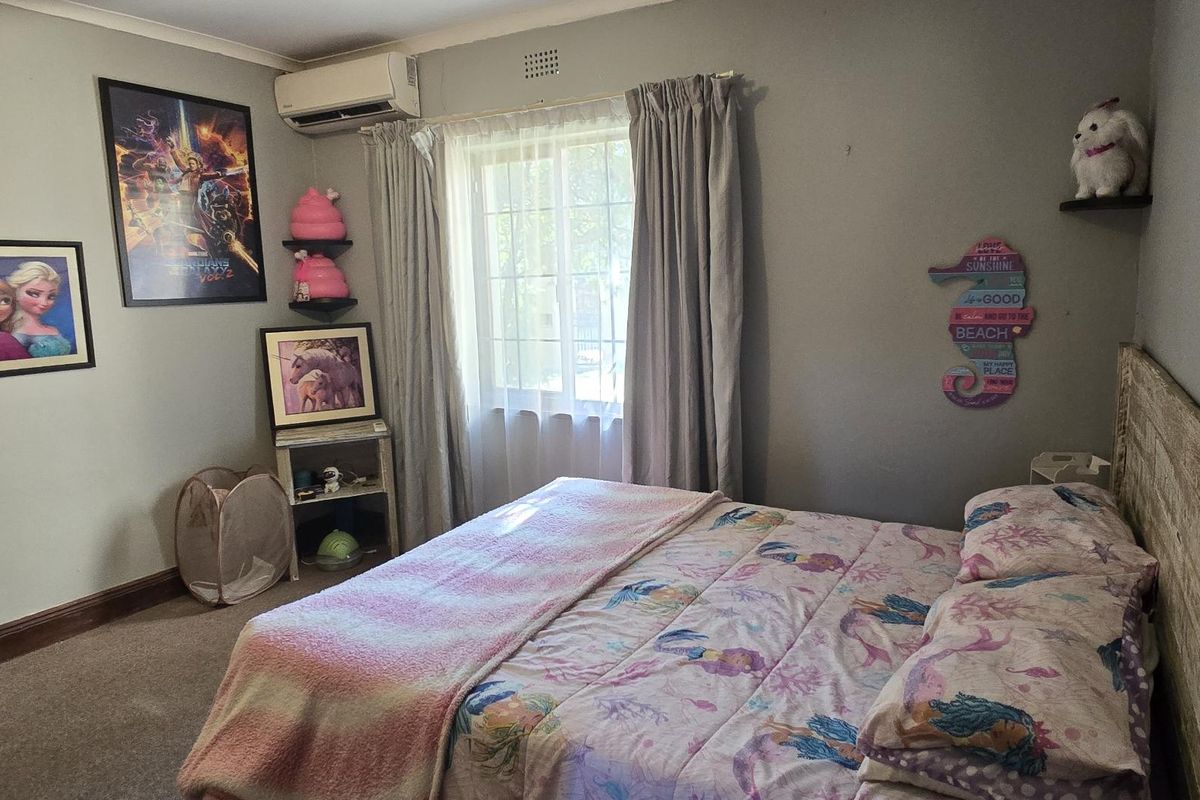 A standard bedroom featuring carpeted flooring, a window with curtains, and a wall-mounted air conditioning unit.