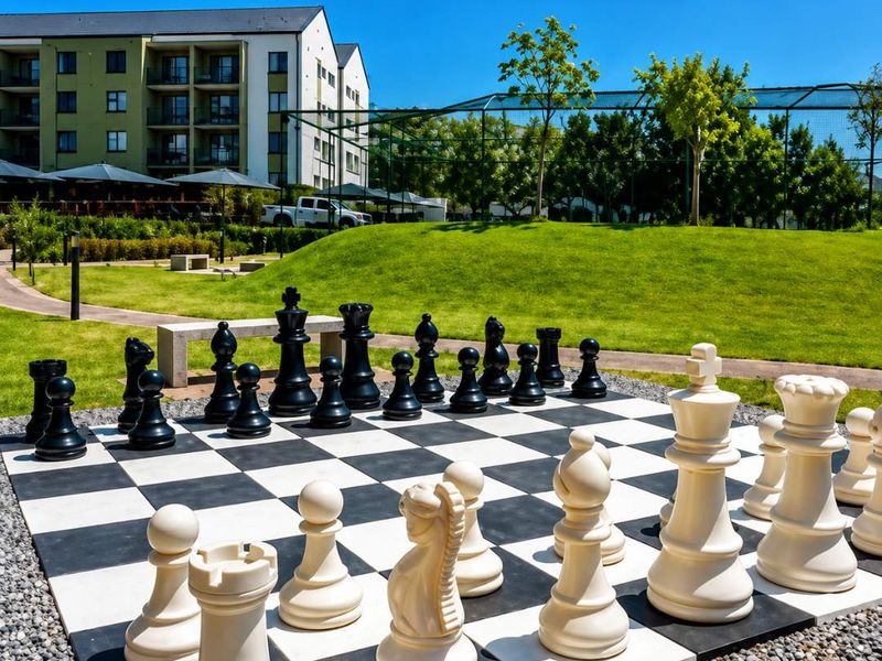 A well-maintained communal garden area featuring a large outdoor chess set, manicured lawns, and paved walkways within an apartment complex.