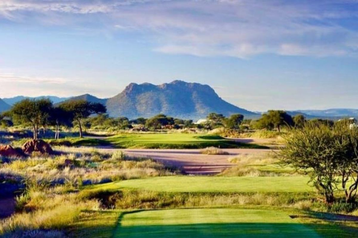 A scenic view of a well-maintained golf course landscape featuring manicured greens, native vegetation, and prominent mountain vistas in the background.