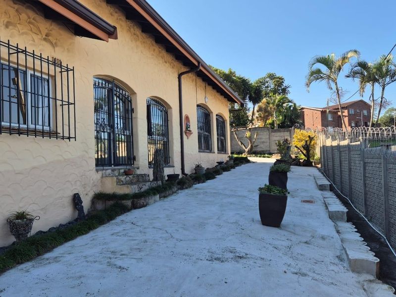 Rear exterior view of the property featuring a concrete driveway, arched windows with security bars, and a secure perimeter boundary wall.