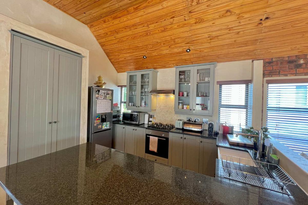 A well-appointed kitchen featuring granite countertops, shaker-style cabinetry, a gas hob with extractor, and a distinctive timber-clad vaulted ceiling with exposed brick accents.