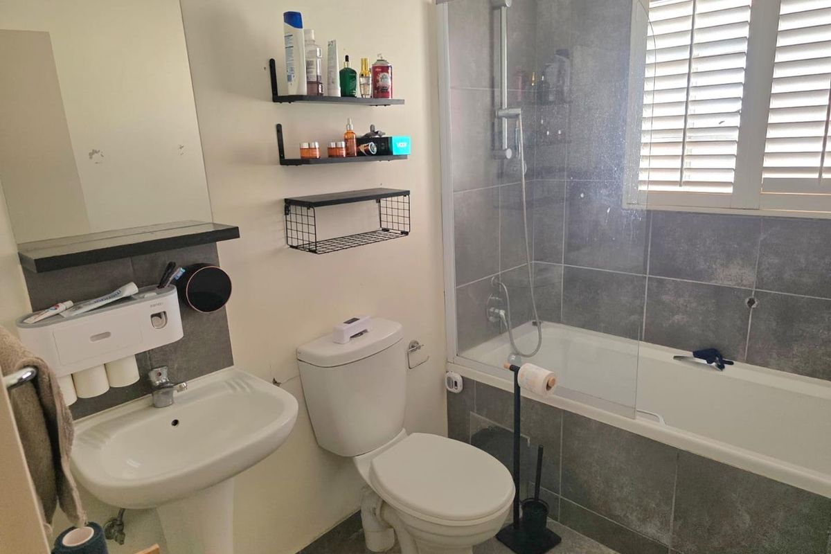 A functional bathroom featuring a pedestal basin, toilet, and a bathtub with a glass shower screen and tiled surround.