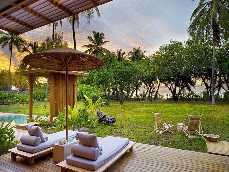 A spacious timber deck featuring an outdoor shower and direct access to a private swimming pool, overlooking a lush tropical garden.