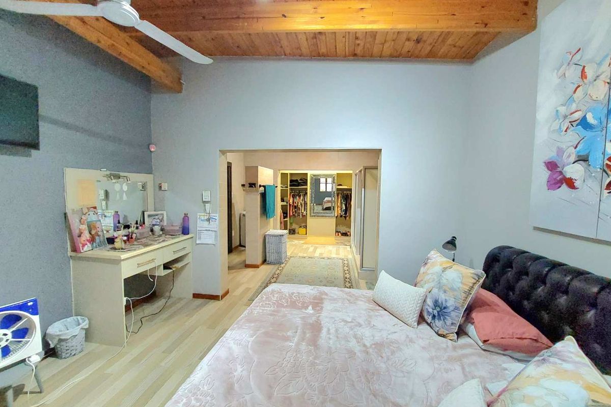 Spacious bedroom featuring exposed timber beam ceilings, light wood-look flooring, and an open-plan walk-in closet area.