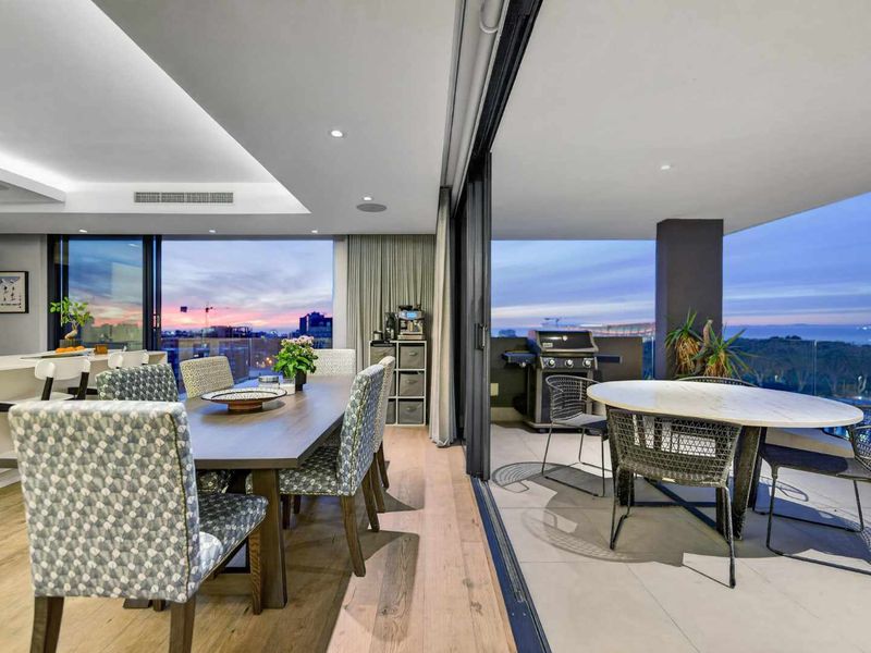 Modern open-plan living and dining area seamlessly flowing onto a spacious covered balcony with panoramic views and integrated lighting.