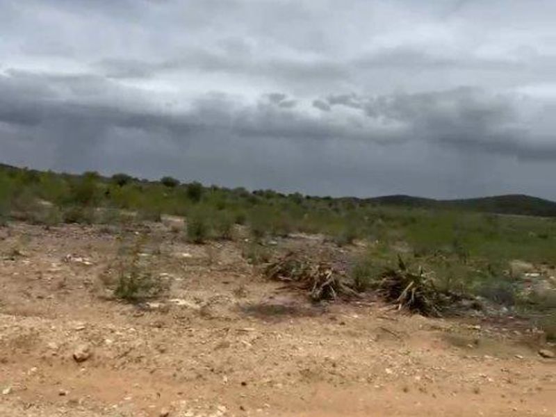 A view of a vacant residential plot featuring natural desert-like terrain and native vegetation under a cloudy sky.