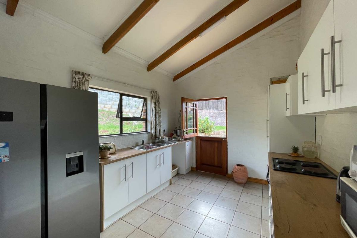 Kitchen featuring exposed timber beams, white cabinetry, laminate countertops, and a stable door leading to the exterior.
