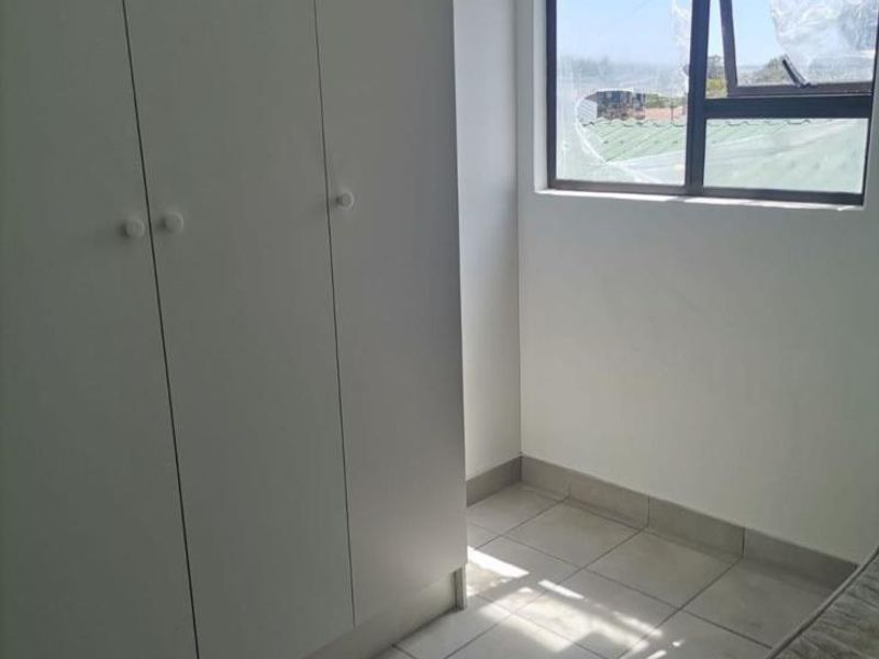 A bright, empty bedroom featuring neutral tiled flooring and a modern built-in wardrobe with clean white finishes.