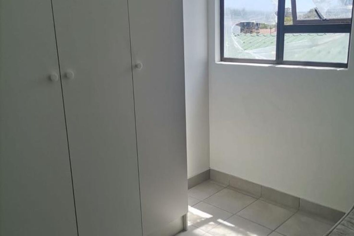 A bright, empty bedroom featuring neutral tiled flooring and a modern built-in wardrobe with clean white finishes.