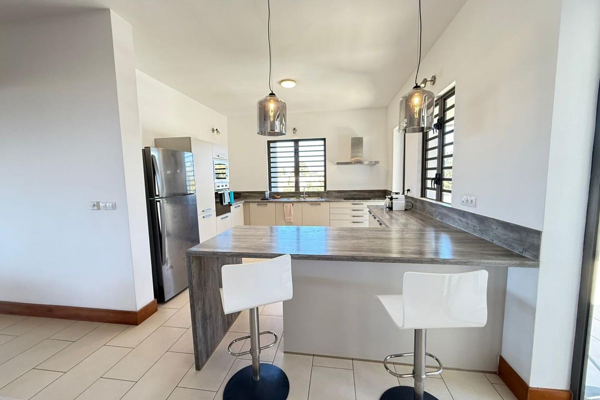 Modern kitchen featuring a breakfast bar, built-in cabinetry, stainless steel extractor fan, and tiled flooring in an open-plan layout.