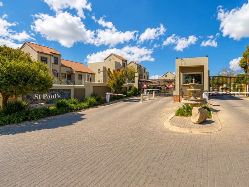 The entrance to St Paul's townhouse complex featuring a paved driveway, security guard house, boom gate access, and landscaped boundary walls.