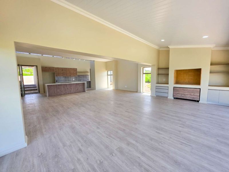 Spacious open-plan living and kitchen area featuring modern cabinetry, light laminate flooring, recessed lighting, and a built-in fireplace alcove in a neutral palette.