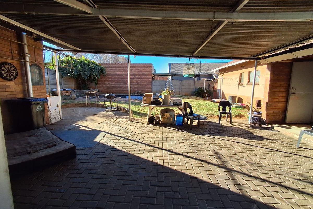 A covered outdoor patio area featuring brick paving and a corrugated metal roof, overlooking a rear garden with brick boundary walls.