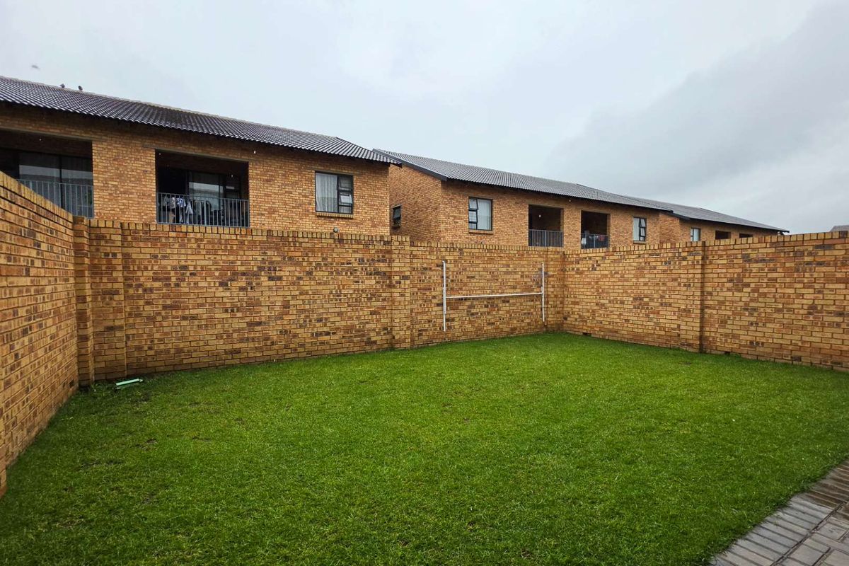 A private rear garden area featuring a lawn and high perimeter face-brick boundary walls, providing a secure outdoor space for the townhouse.
