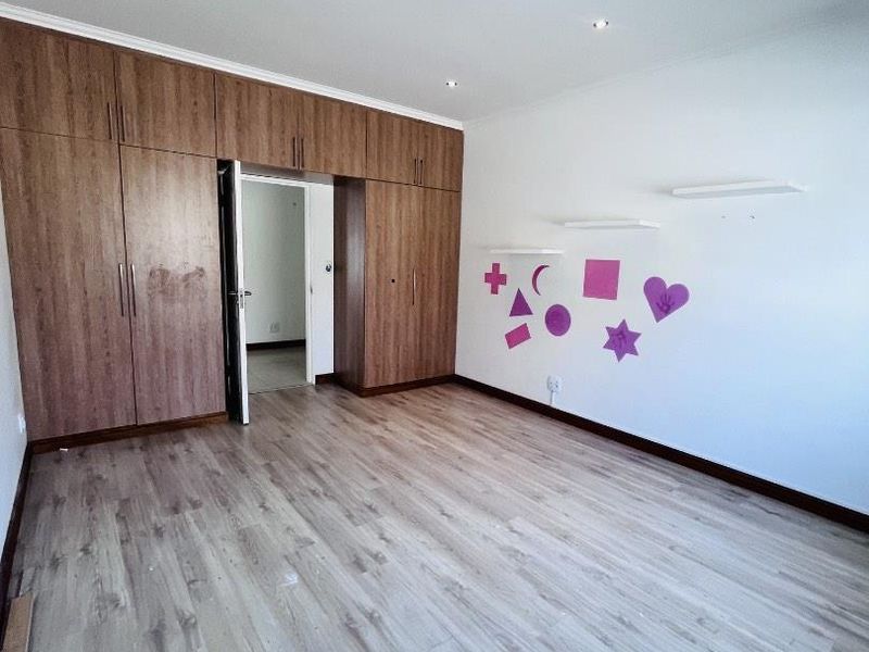 Spacious bedroom featuring extensive built-in wooden cupboards, modern laminate flooring, and recessed ceiling lighting.