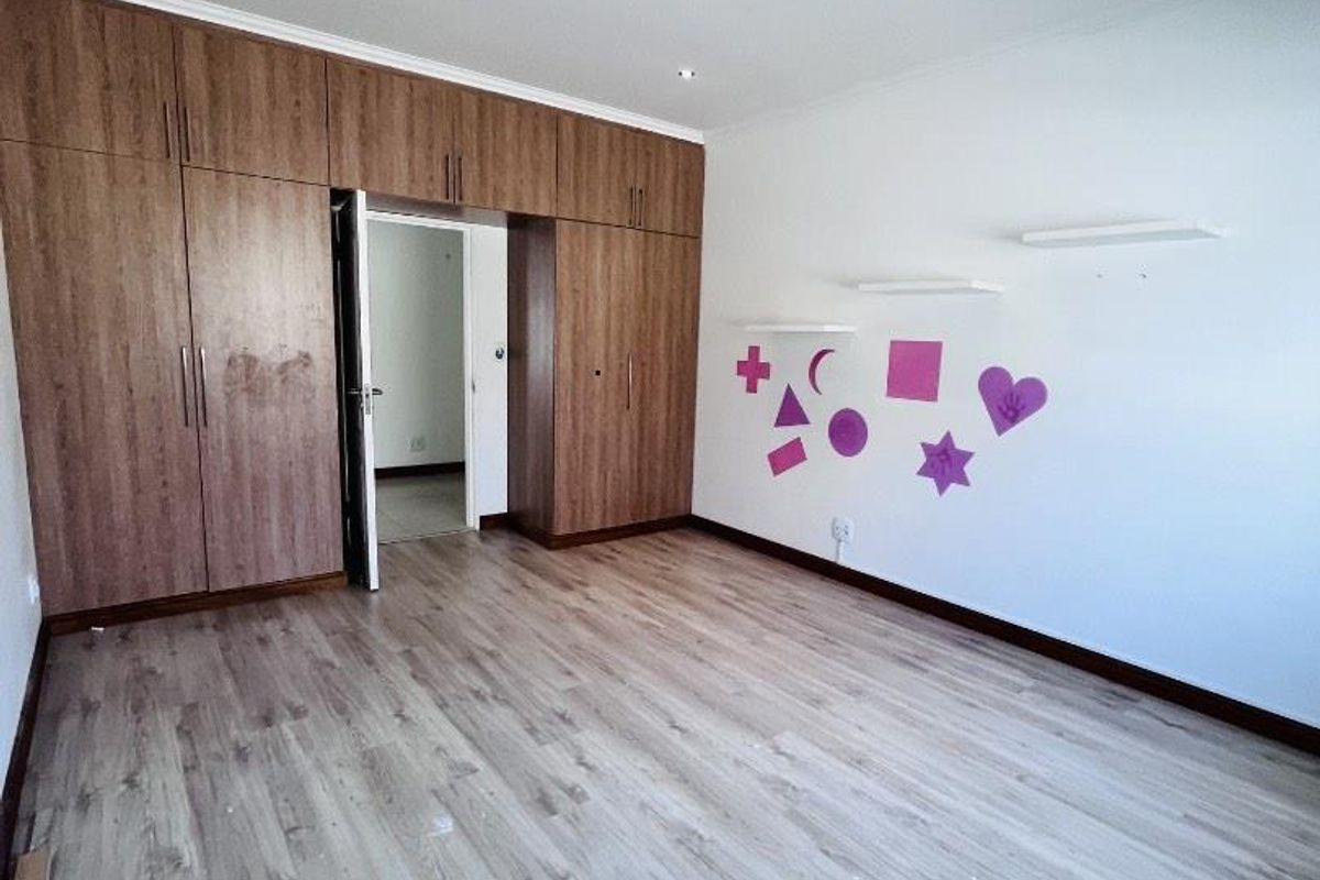 Spacious bedroom featuring extensive built-in wooden cupboards, modern laminate flooring, and recessed ceiling lighting.