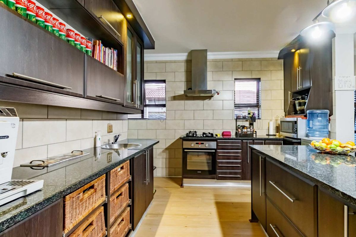 Modern kitchen featuring dark wood cabinetry, granite countertops, stainless steel oven, gas hob, and extractor fan with tiled backsplash.