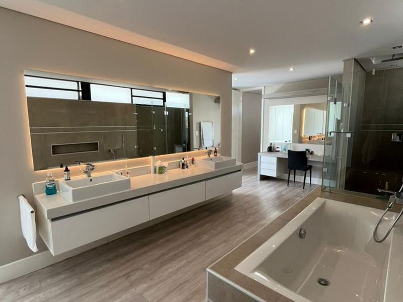 Modern, spacious bathroom featuring a double vanity with backlit mirror, built-in bathtub, glass-enclosed shower, and integrated dressing area with high-quality finishes.
