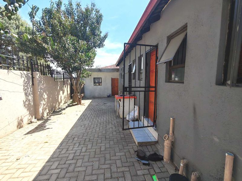 Rear exterior view of the property featuring a paved courtyard, security gate, and boundary wall.
