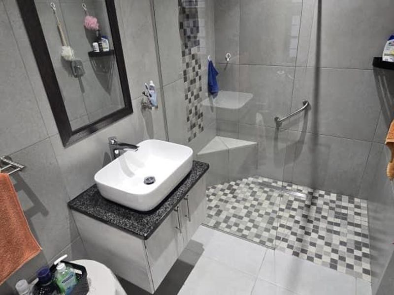 Modern bathroom featuring a vessel sink on a granite-topped vanity and a walk-in shower with a built-in seat and mosaic tile accents.
