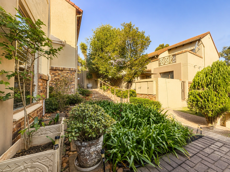 A well-maintained rear exterior view of the townhouse featuring brick paving, stone stairs with a metal handrail, and established garden landscaping.