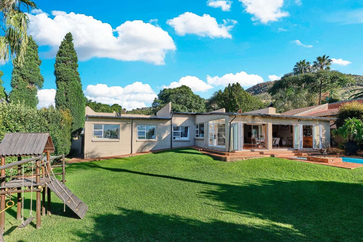Rear view of the property featuring a spacious lawn, swimming pool, and a covered patio area with folding glass doors for indoor-outdoor flow.