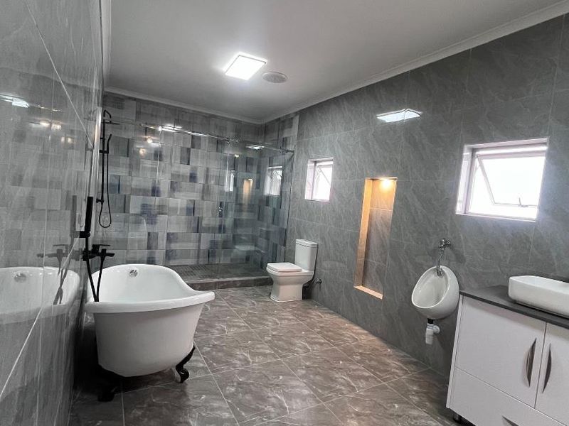 Modern bathroom featuring a freestanding bathtub, walk-in glass shower, wall-mounted toilet, urinal, and a vanity with a vessel sink, finished with grey marble-look tiles.