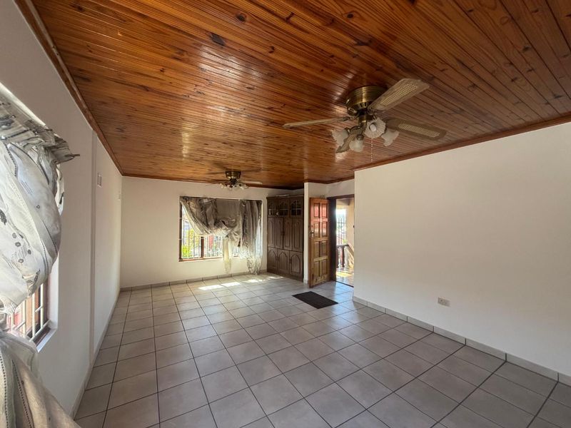 Spacious living area featuring a warm timber tongue and groove ceiling, neutral ceramic floor tiles, and built-in wooden storage cabinetry.