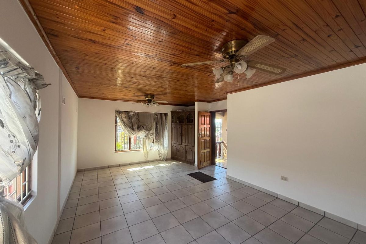 Spacious living area featuring a warm timber tongue and groove ceiling, neutral ceramic floor tiles, and built-in wooden storage cabinetry.