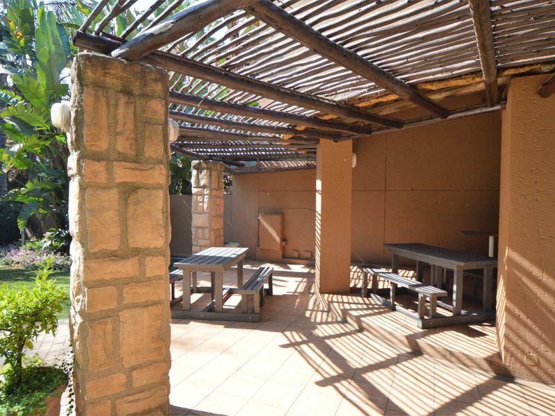 Covered outdoor patio area featuring stone-clad pillars, a timber pergola roof, and tiled flooring, overlooking a garden space.