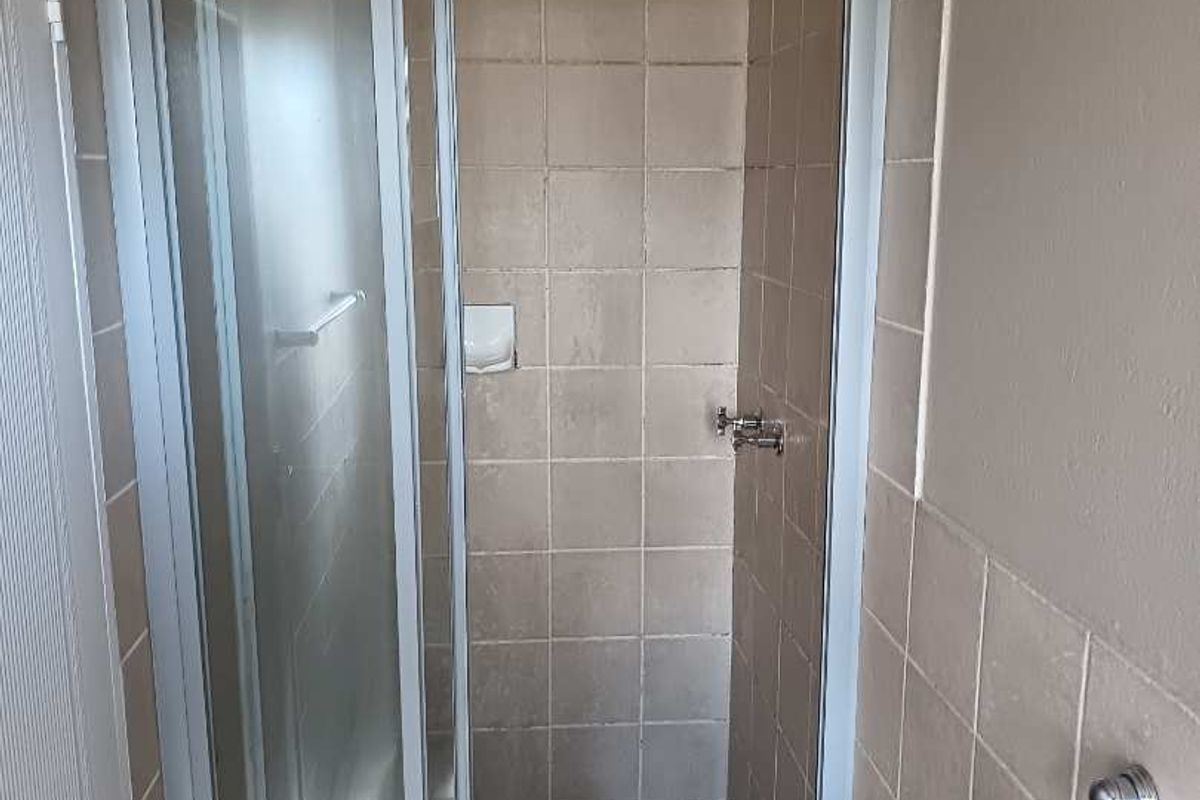 A functional shower stall featuring tiled walls, a glass enclosure, and a tiled floor, requiring minor cosmetic updates to refresh the space.