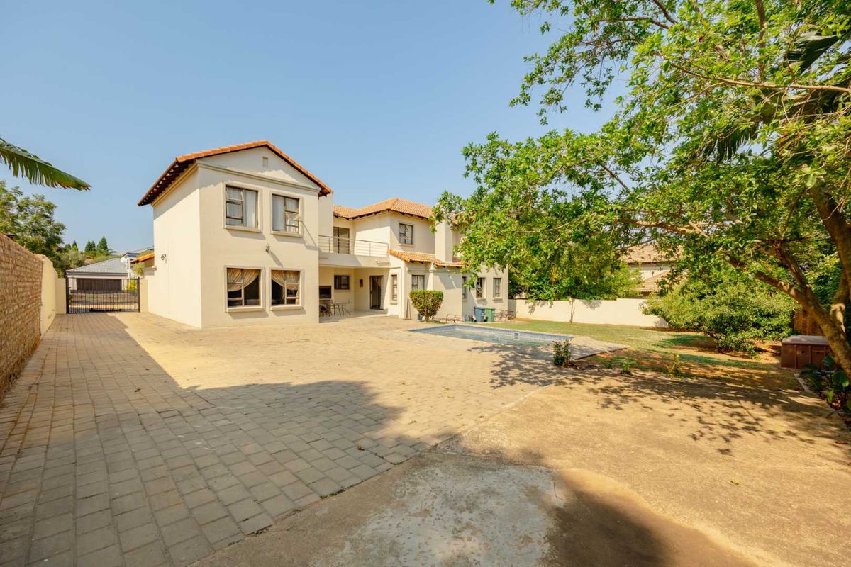 Rear view of a two-story house featuring a swimming pool, paved courtyard, balcony, and established garden area.