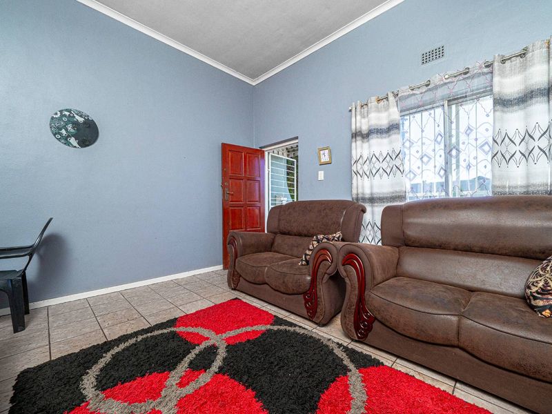A living room featuring tiled flooring, blue painted walls, and a sliding window with security bars.