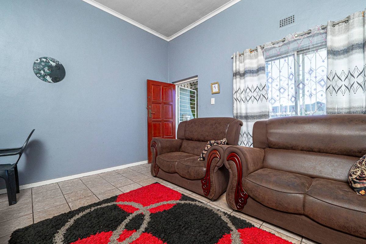 A living room featuring tiled flooring, blue painted walls, and a sliding window with security bars.