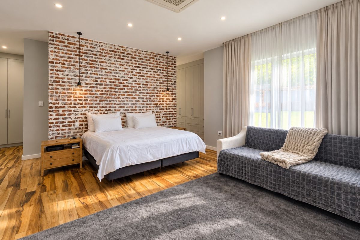 Spacious bedroom featuring an exposed brick feature wall, built-in cabinetry, timber flooring, and integrated ducted air conditioning.