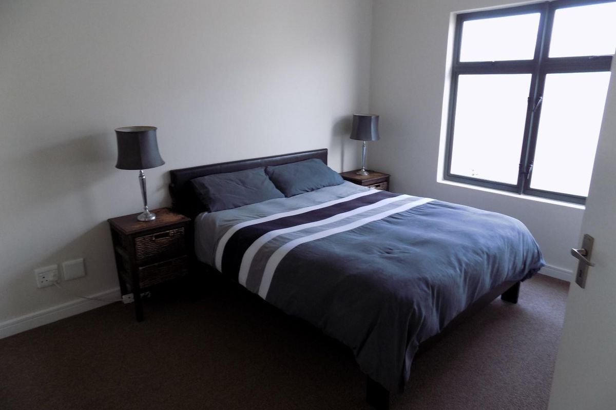 A well-maintained bedroom featuring neutral wall tones, carpeted flooring, and a large window providing natural light.