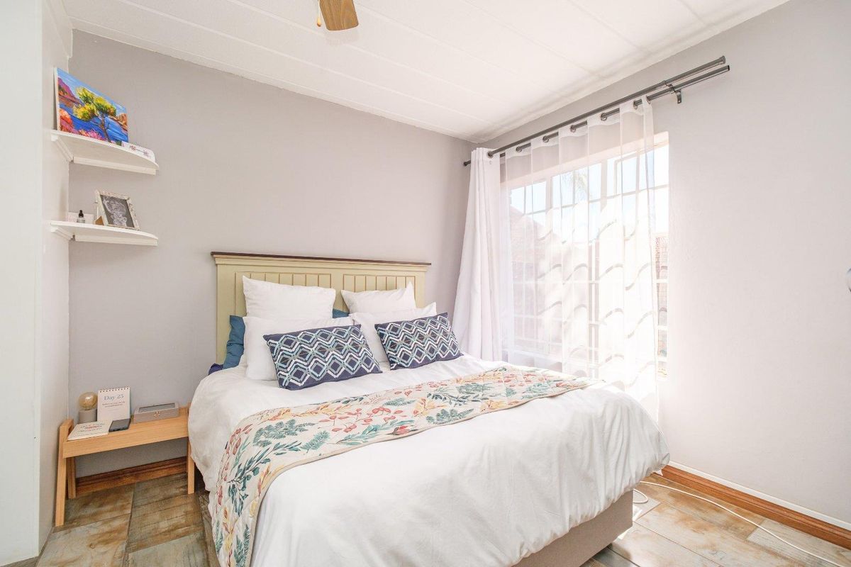 A bright and cozy bedroom featuring a ceiling fan, natural light from the window, and built-in floating shelving.