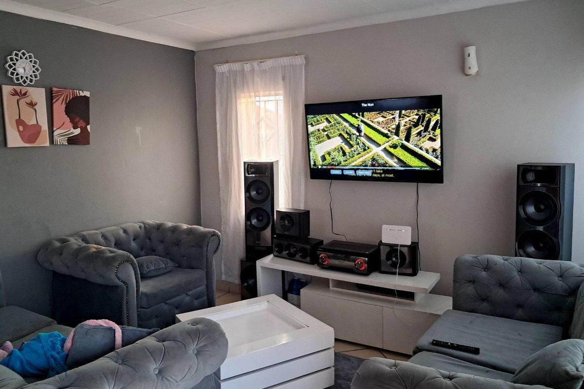 A comfortable living room featuring a wall-mounted television, neutral grey walls, and tiled ceiling finishes.