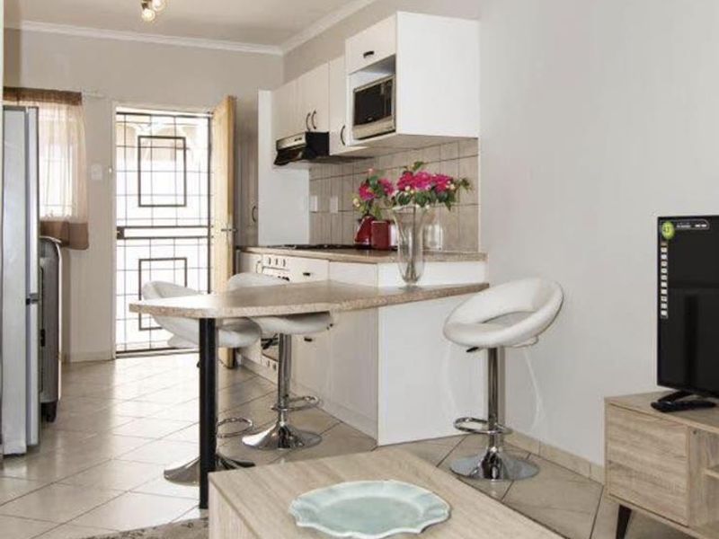 Open-plan living area featuring a compact kitchen with built-in cabinetry, breakfast bar, and tiled flooring, leading to an exterior security door.