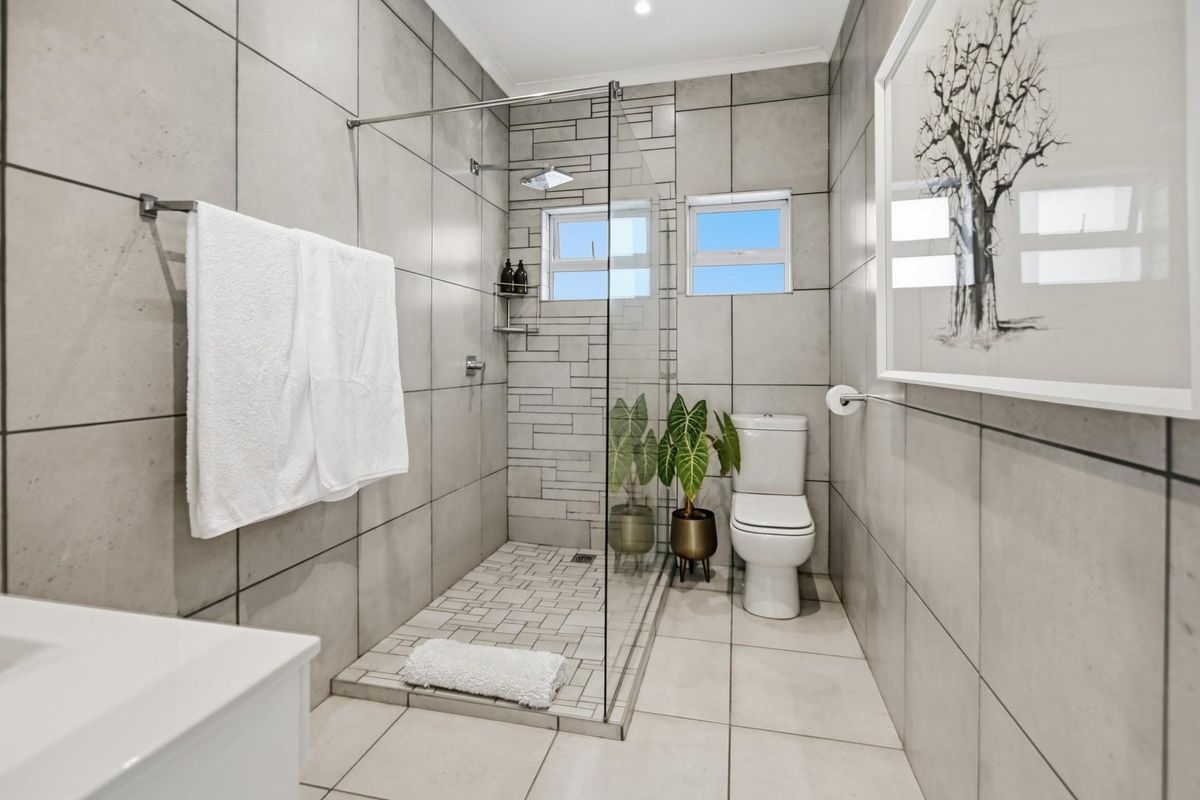 Modern bathroom featuring a spacious walk-in shower with a glass screen, rain shower head, and contemporary grey tiling throughout.