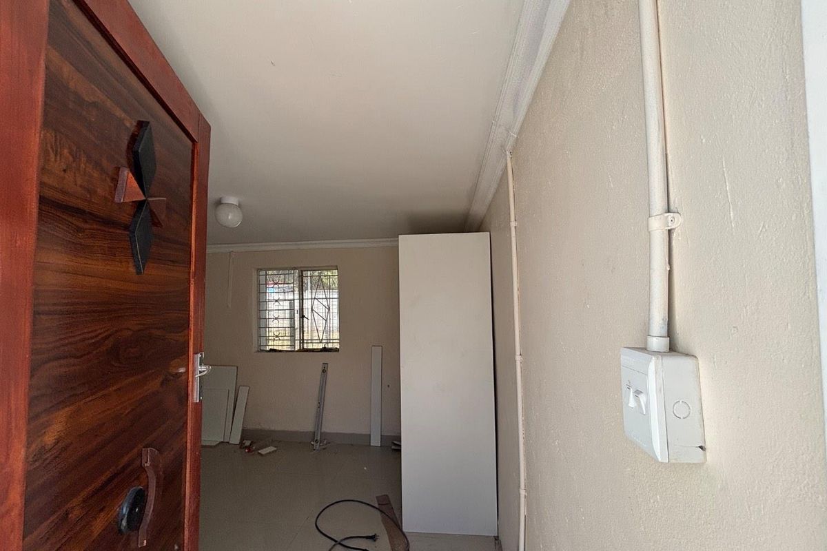 An empty bedroom featuring a timber entrance door, security bars on the window, and visible surface-mounted electrical conduit.