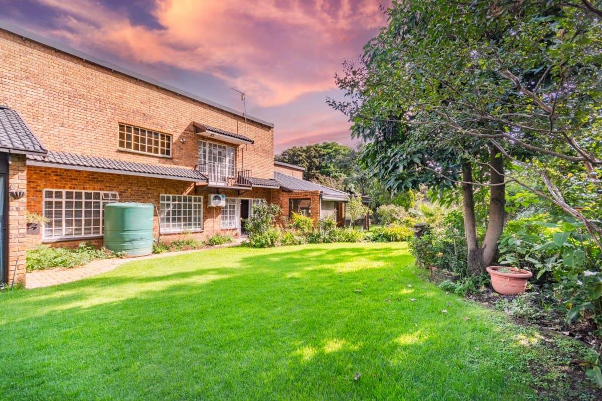 A view of the rear brick facade of the house, featuring a well-maintained lawn, established garden, and a large water storage tank.