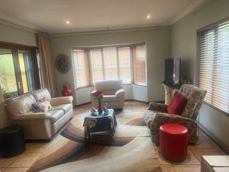 A comfortable living room featuring tiled flooring, a prominent bay window with timber blinds, and recessed downlighting, providing a bright and functional space.